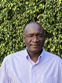 A man wearing glasses and a blue shirt is standing in front of a bush.
