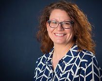 A woman wearing glasses and a blue and white shirt is smiling for the camera.
