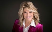 A woman in a pink jacket and white shirt is smiling for the camera.