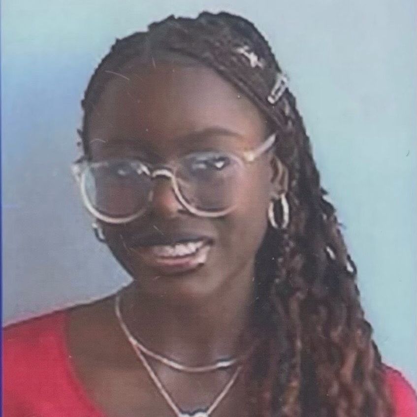A woman wearing glasses and a necklace is smiling for the camera.
