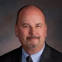 A bald man with a beard is wearing a suit and tie.