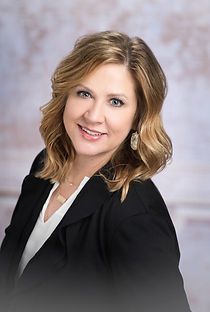 A woman in a black jacket and white shirt is smiling for the camera.