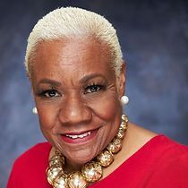 A woman wearing a red shirt and a gold necklace is smiling for the camera.