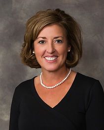 A woman wearing a black shirt and a pearl necklace is smiling for the camera.