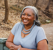 A woman is smiling while sitting on a bench in the woods.