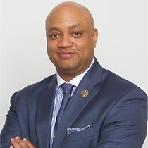 A bald man in a suit and tie is standing with his arms crossed.