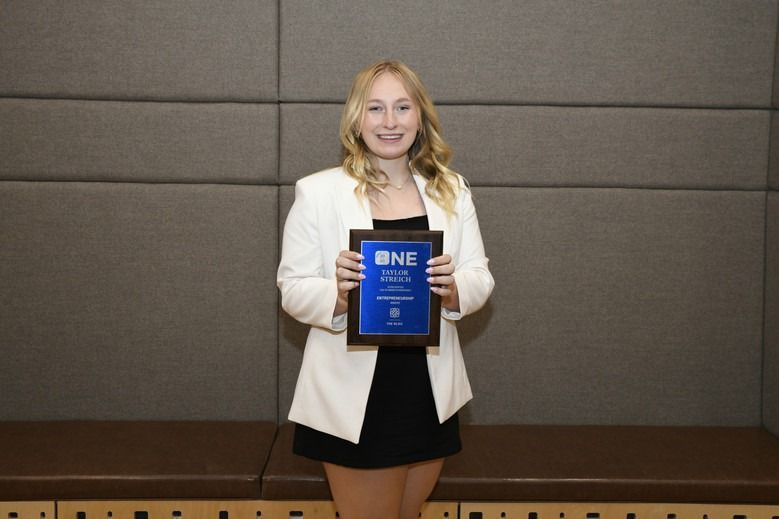 A woman in a white jacket is holding a plaque that says bne