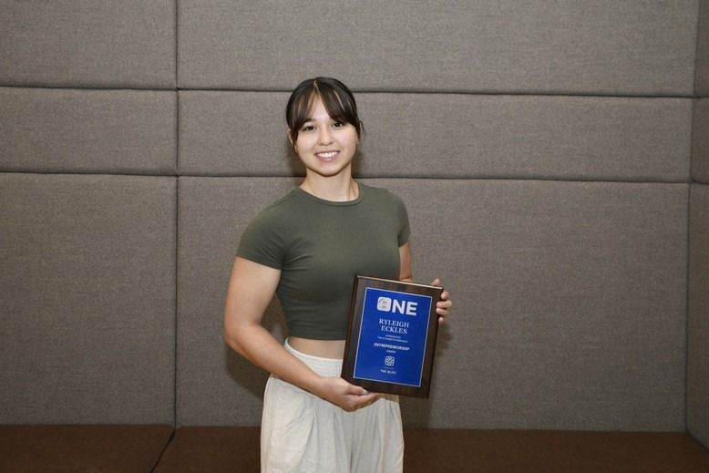 A woman is holding a plaque in front of a wall.