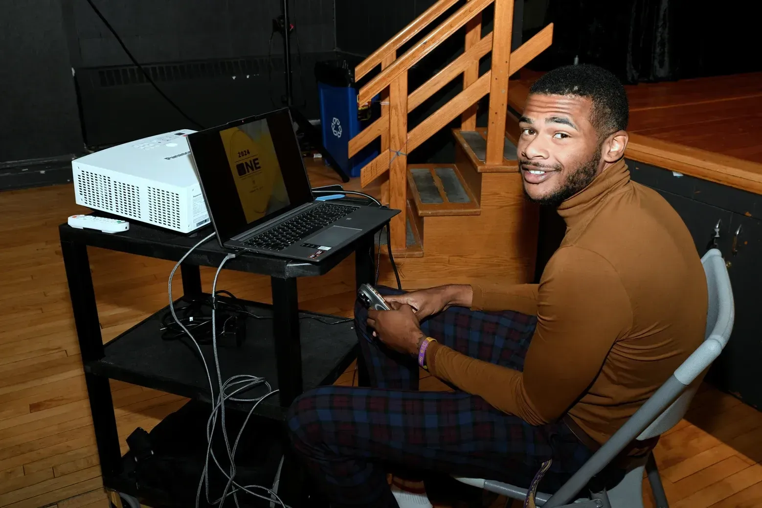 A man is sitting in a chair in front of a laptop and a projector.