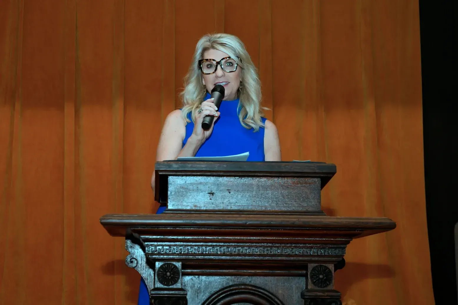 A woman is standing at a podium holding a microphone.