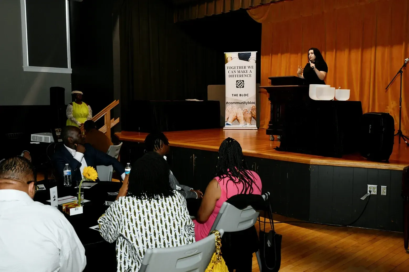 A woman is standing on a stage giving a presentation to a group of people.