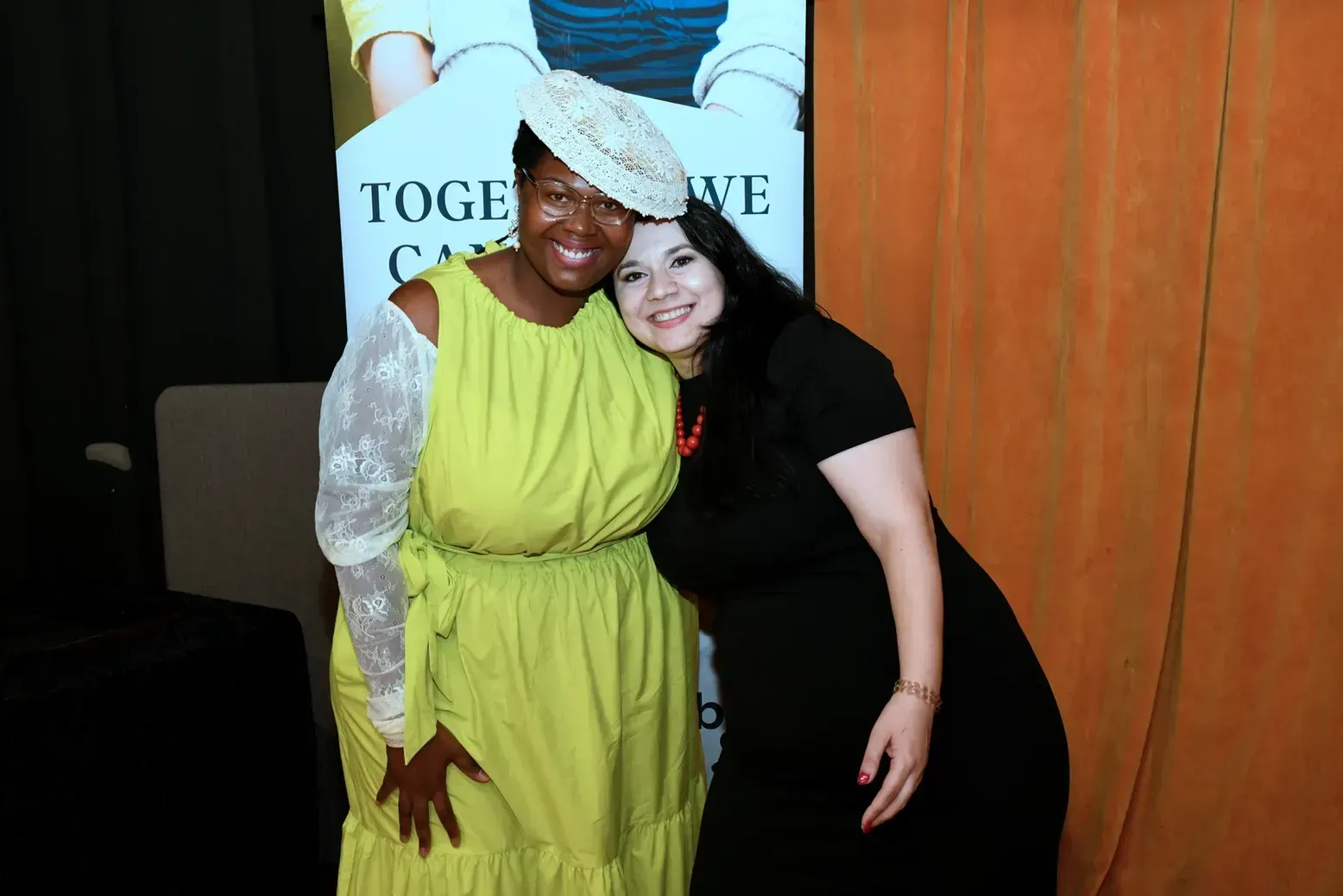 Two women are posing for a picture in front of a sign that says together