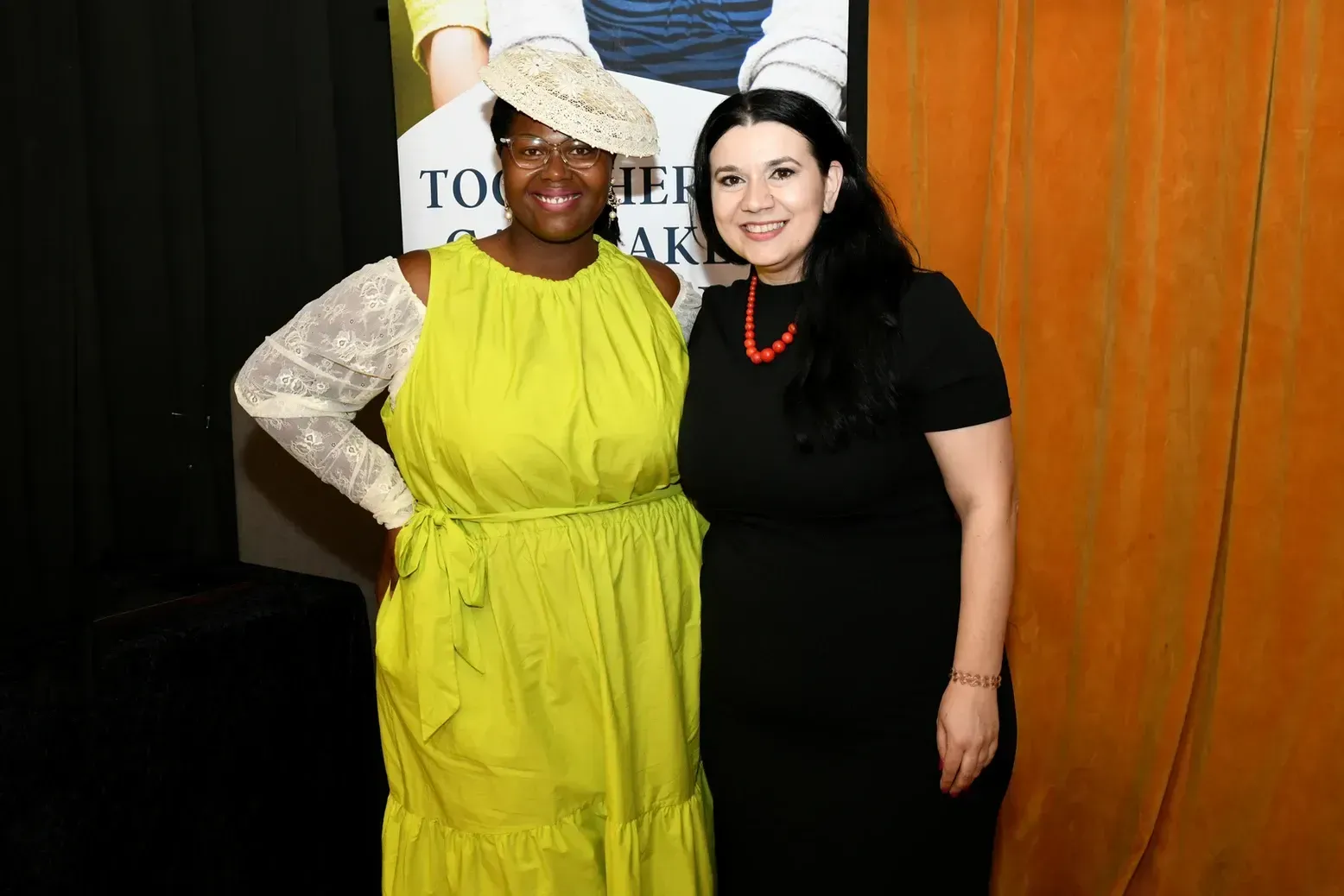 Two women are posing for a picture together . one is wearing a yellow dress and the other is wearing a black dress.
