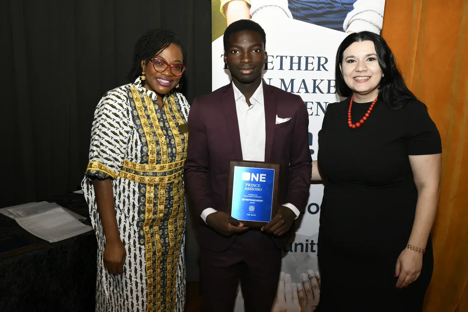 A man in a suit is standing between two women holding a plaque.