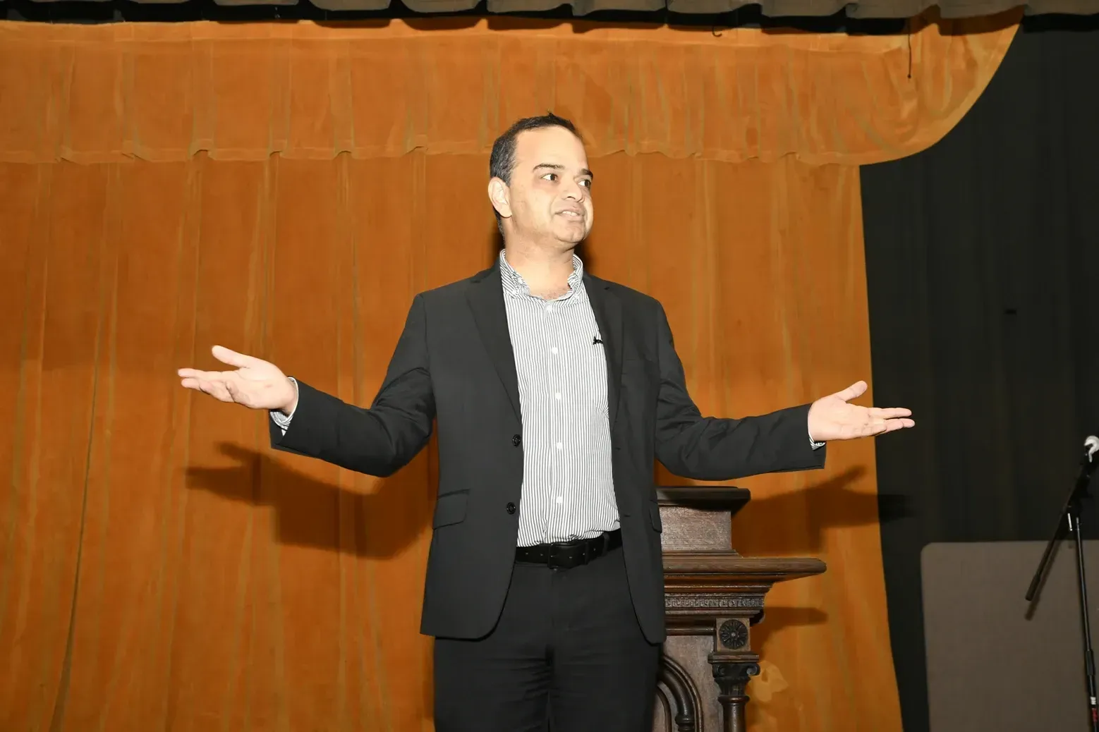 A man in a suit is standing in front of a podium with his arms outstretched.