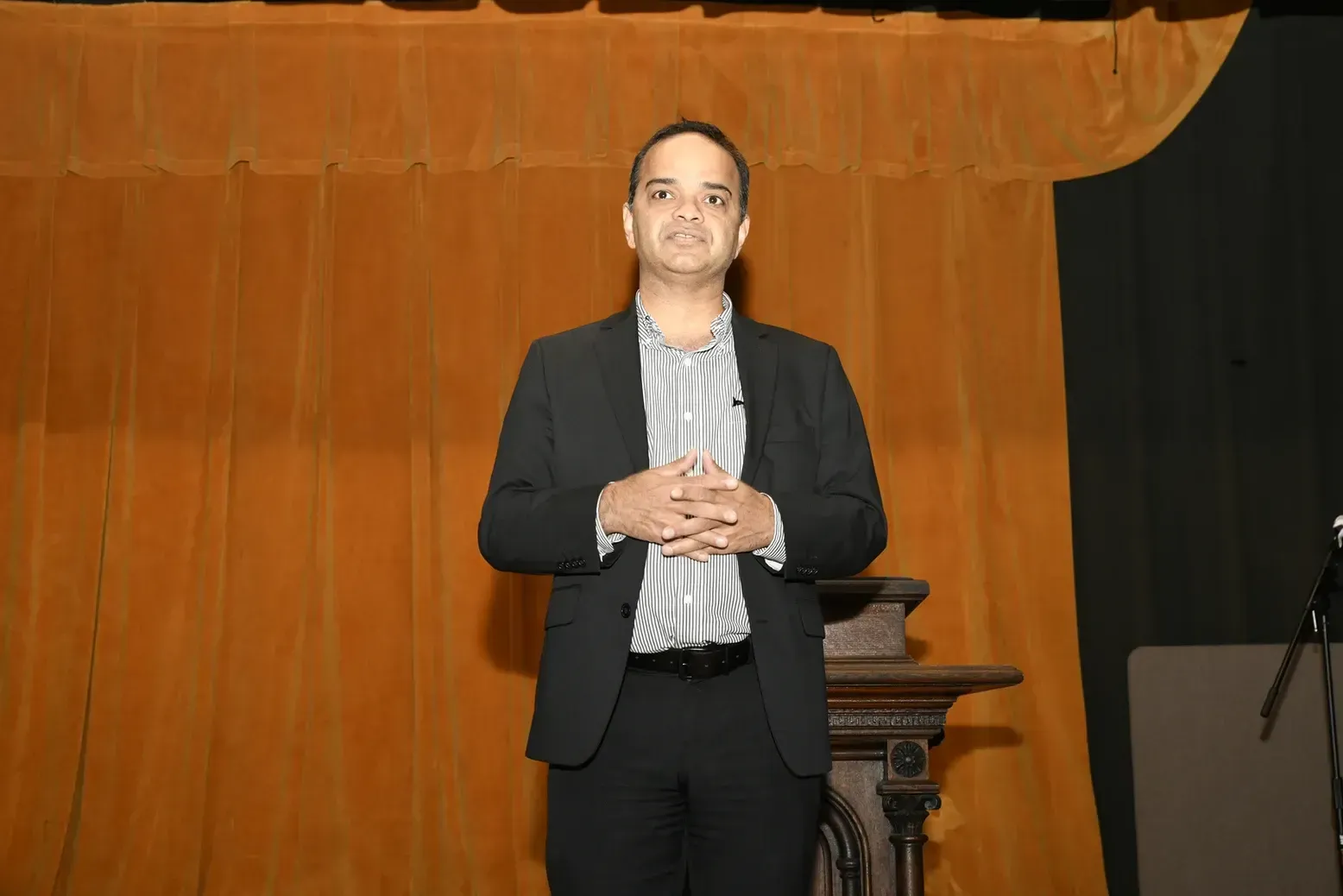 A man in a suit is standing in front of a wooden wall.