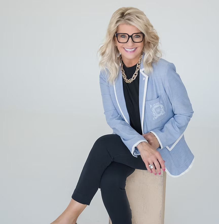 A woman wearing glasses and a blue jacket is sitting on a chair