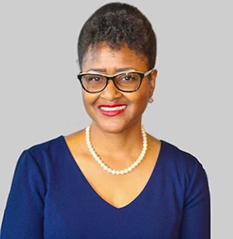 A woman wearing glasses and a pearl necklace is smiling for the camera.