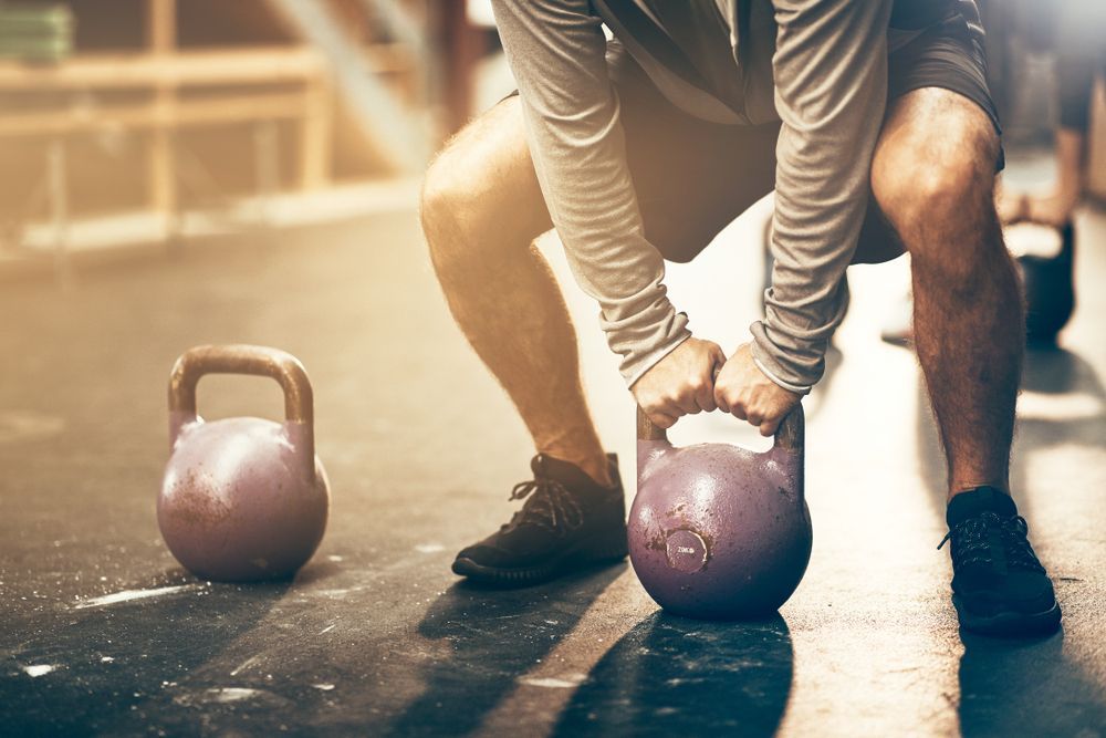 Person Gripping a Purple Kettlebell on a Gym Floor — Forerunner Physio In Taree, NSW