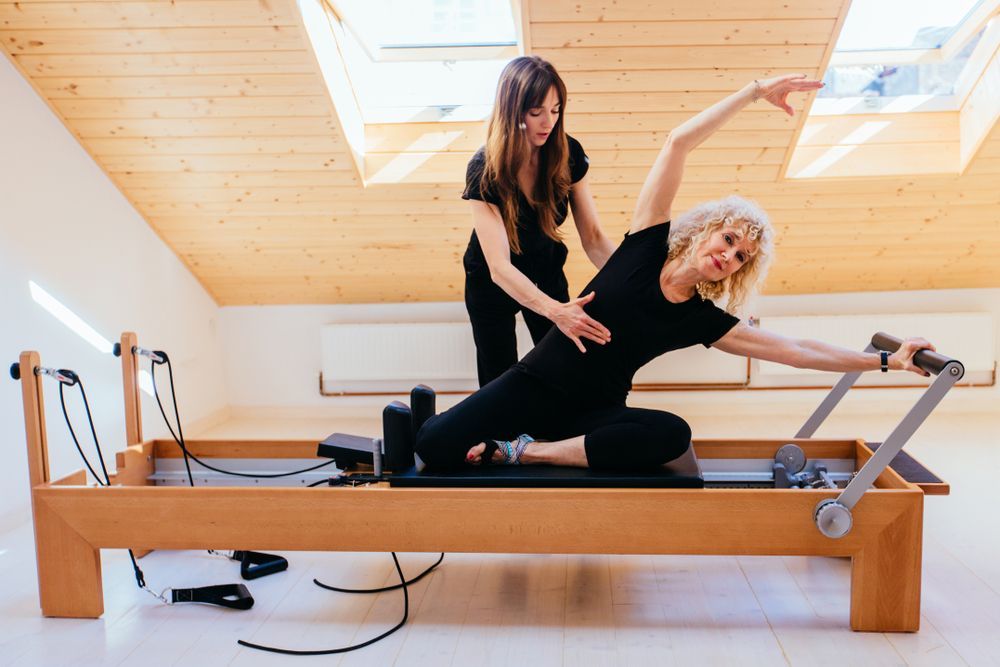 Woman Doing Pilates With Instructor's Help — Forerunner Physio In Taree, NSW