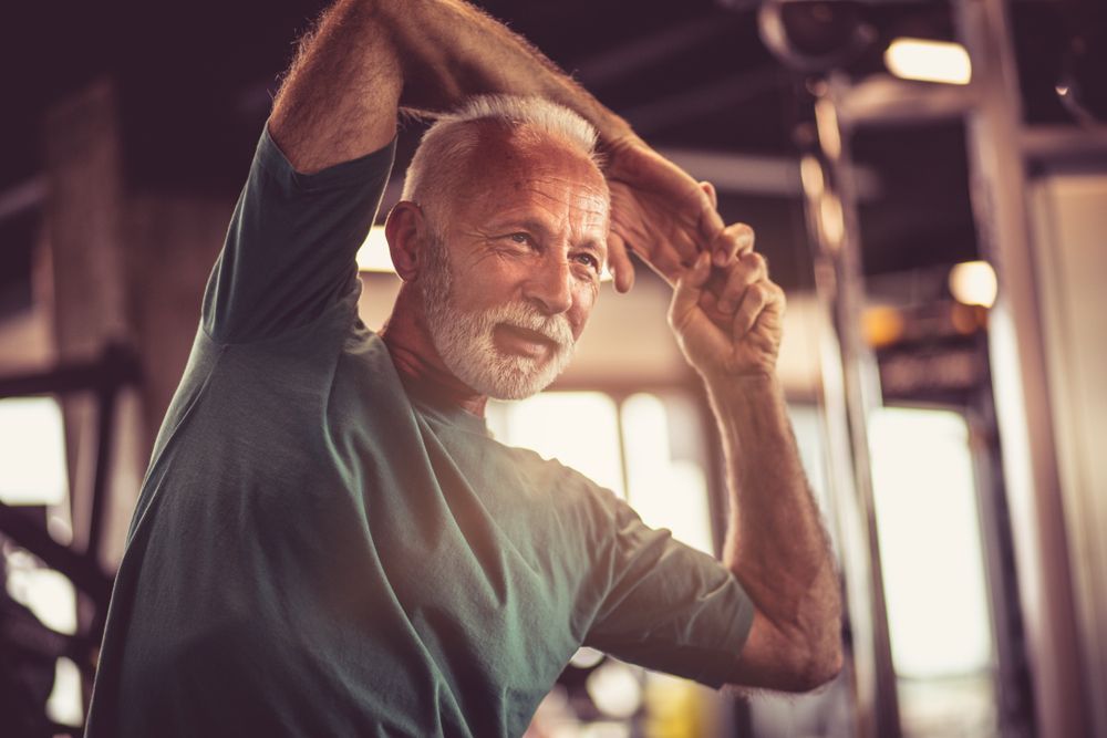 Senior Man Stretching Arms in a Gym, Smiling, Wearing a Green Shirt — Forerunner Physio In Taree, NSW