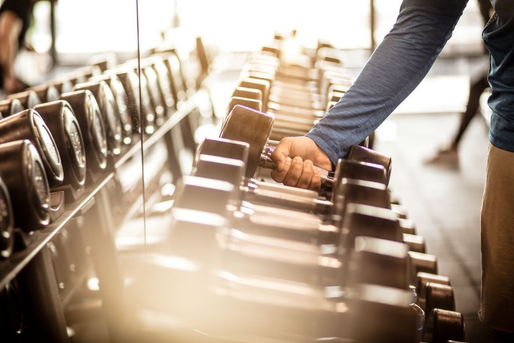 Person's Hand Reaching for a Dumbbell on a Rack Inside a Gym — Forerunner Physio In Taree, NSW