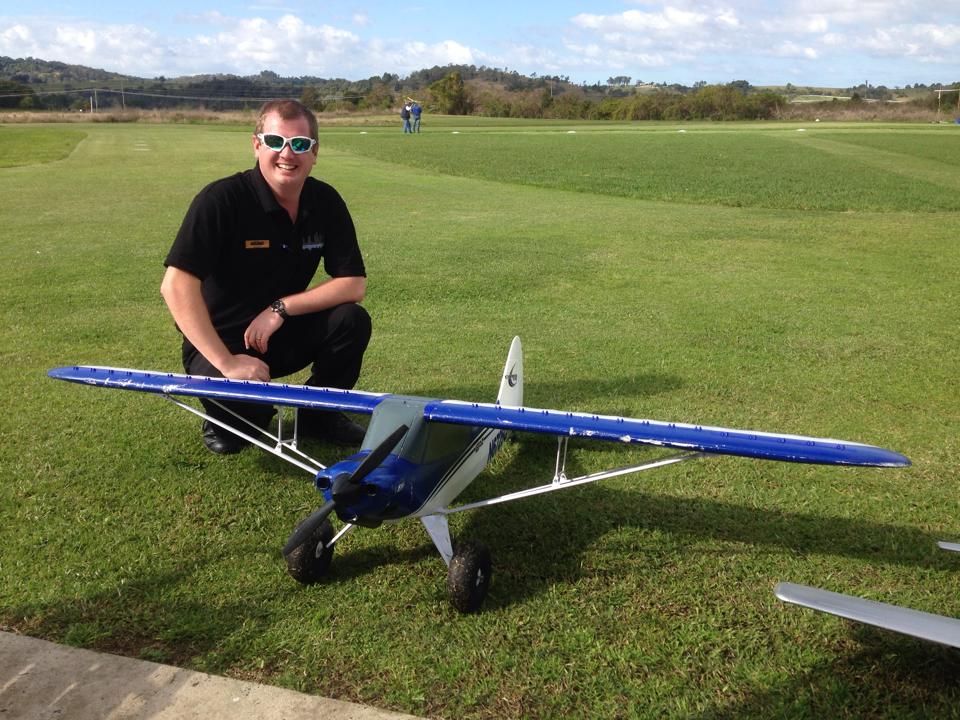 Man eith sunglasses kneeling in field next to Model Airplane With Propeller— Midtown Hobbies In Lismore, NSW