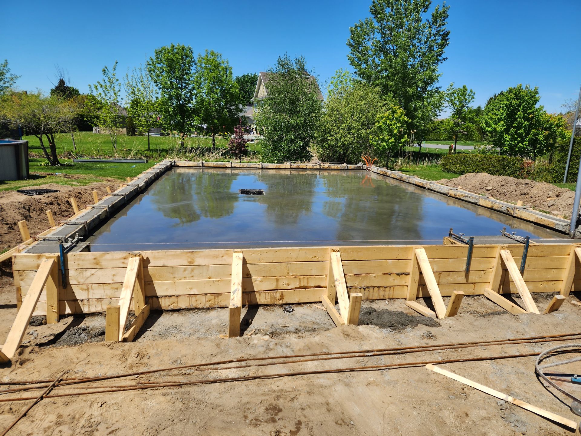 Une fondation en béton est en cours de construction dans une cour avec des coffrages en bois.