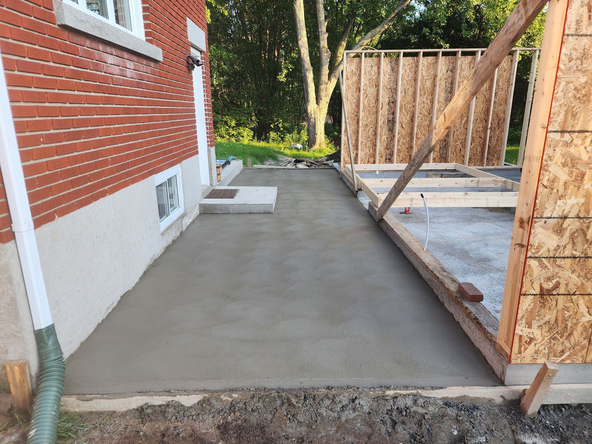 Une passerelle en béton est en cours de construction devant une maison en briques.