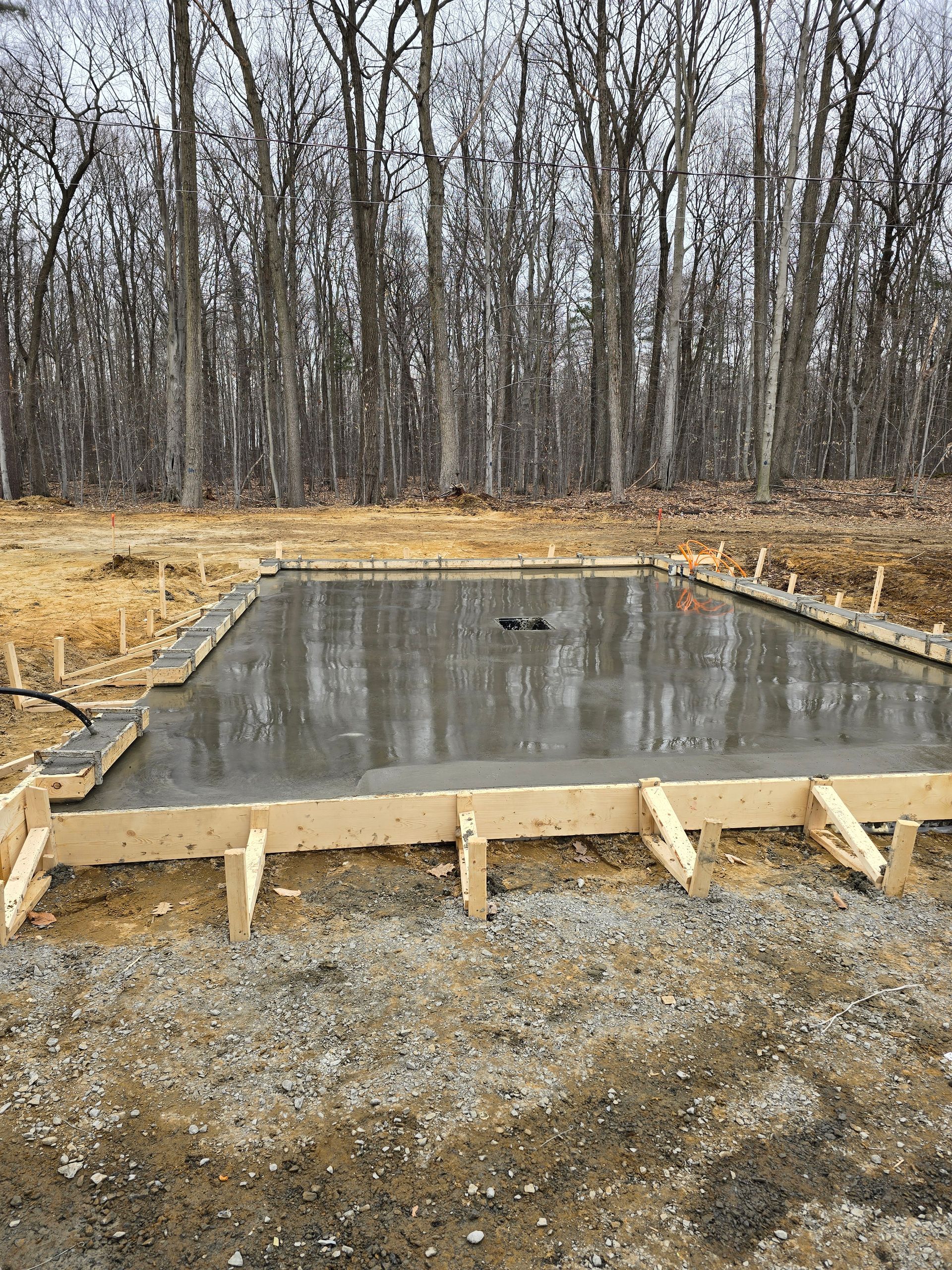 Une fondation en béton est en cours de construction dans un champ avec des arbres en arrière-plan.