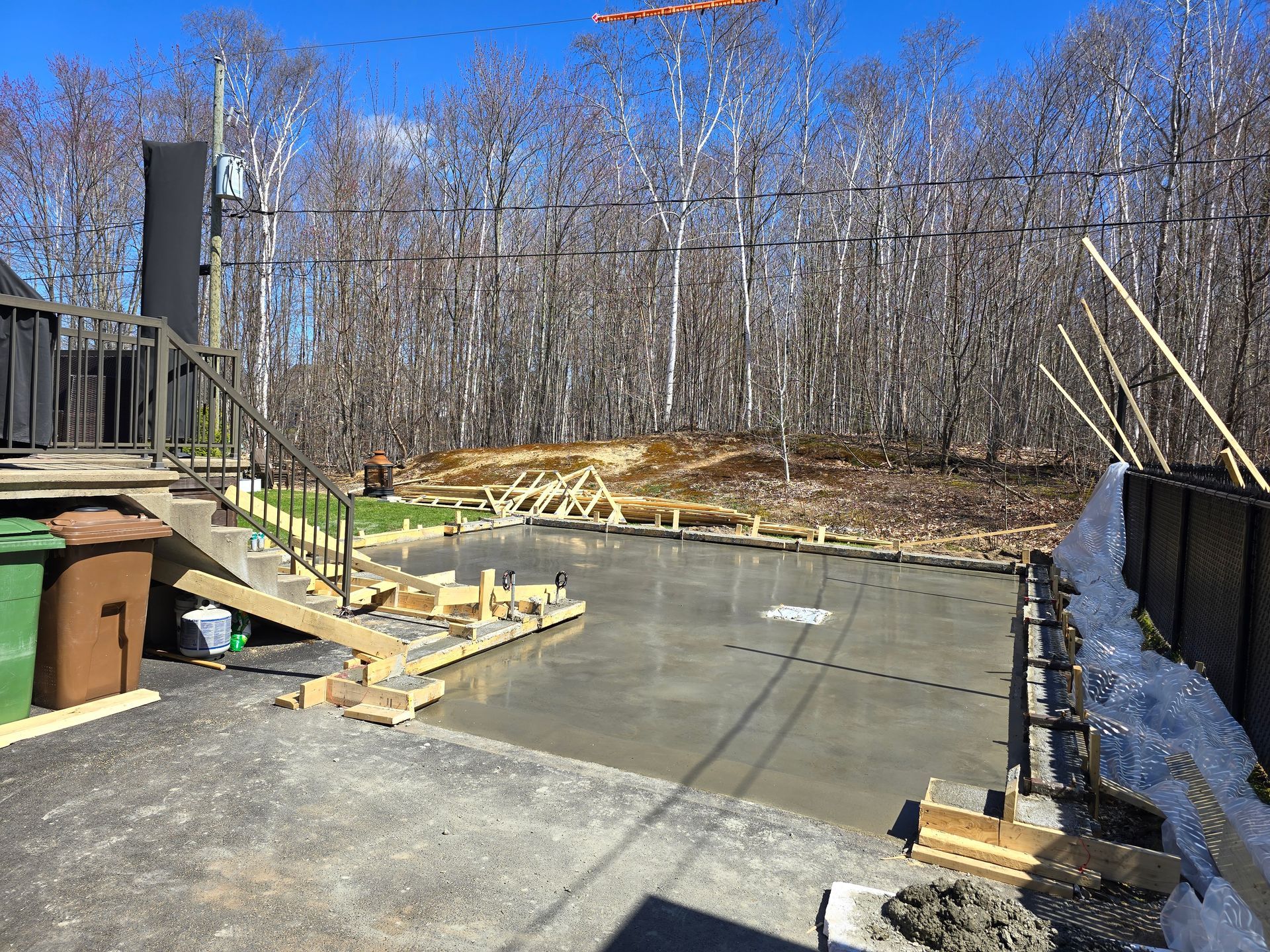 Un sol en béton est en cours de construction dans une cour arrière avec des arbres en arrière-plan.