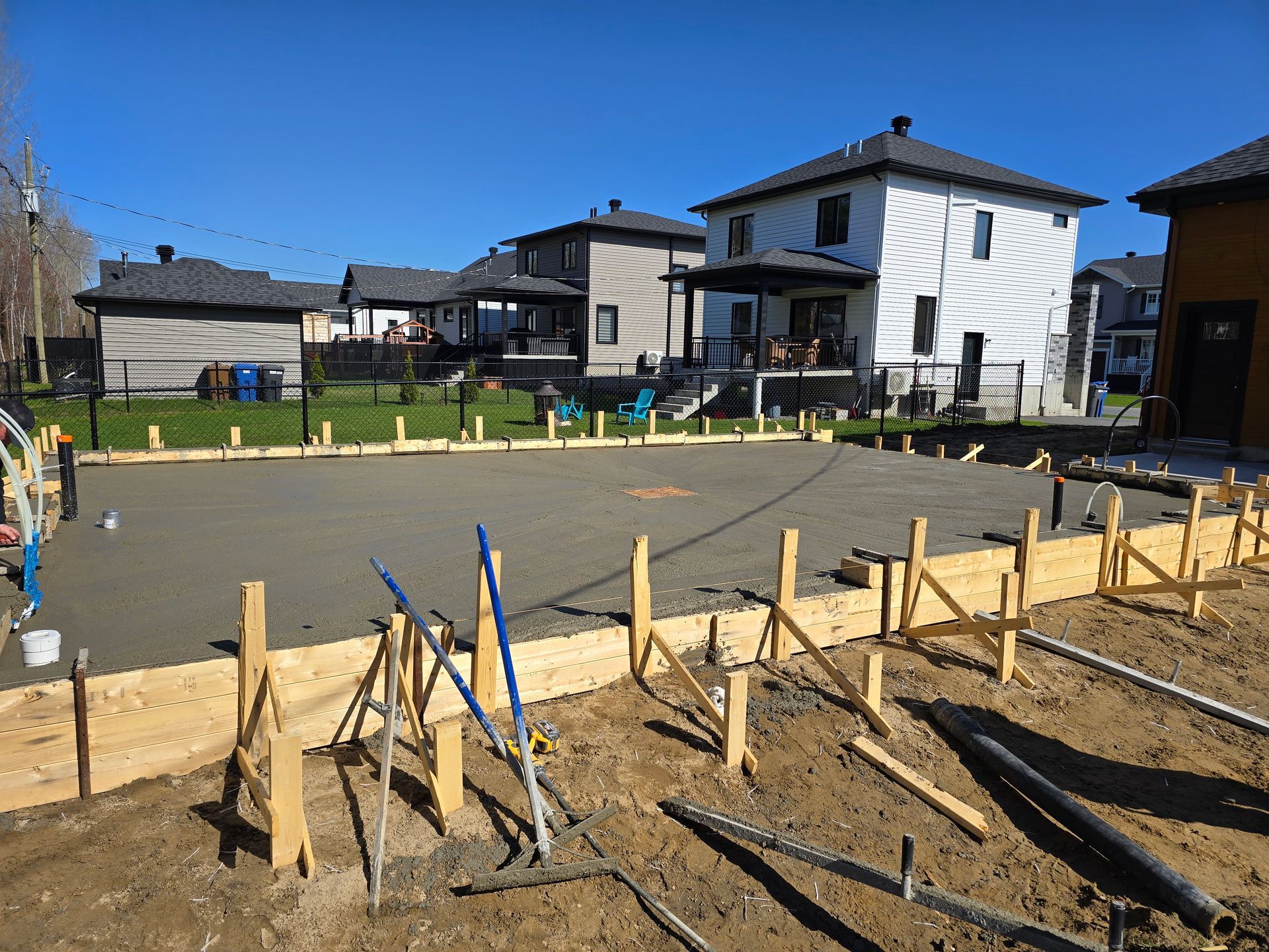 Une dalle de béton est en train d'être coulée devant une maison en construction.