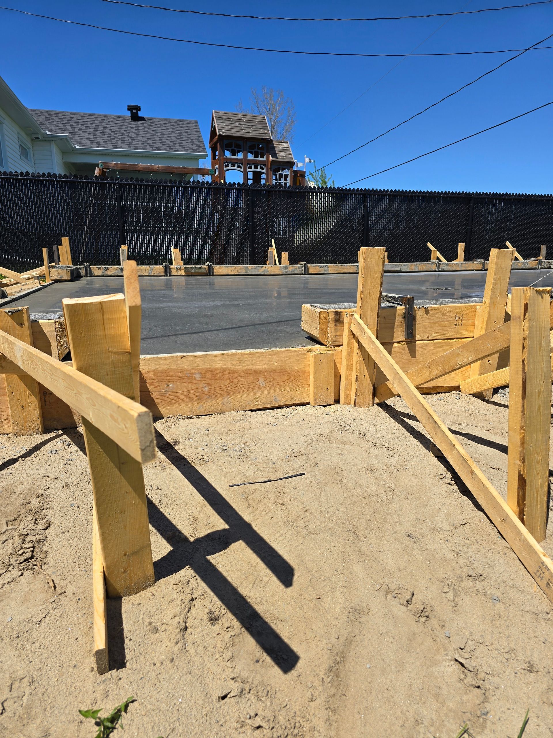 Une clôture en bois est en train d'être construite dans le sable avec une maison en arrière-plan