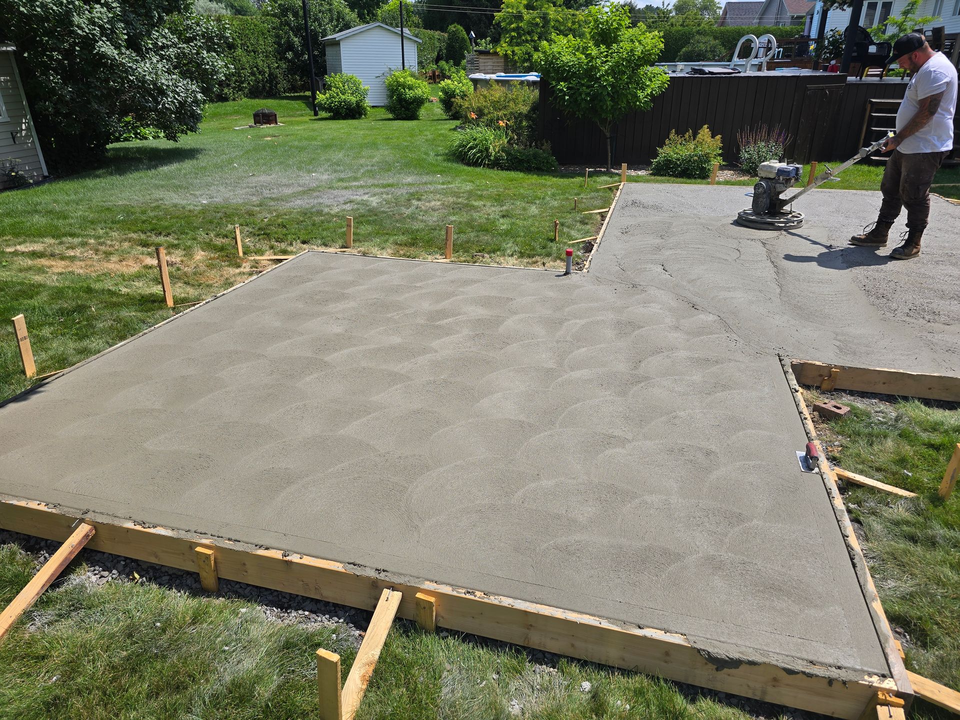 Un homme travaille sur une allée en béton dans une cour arrière.