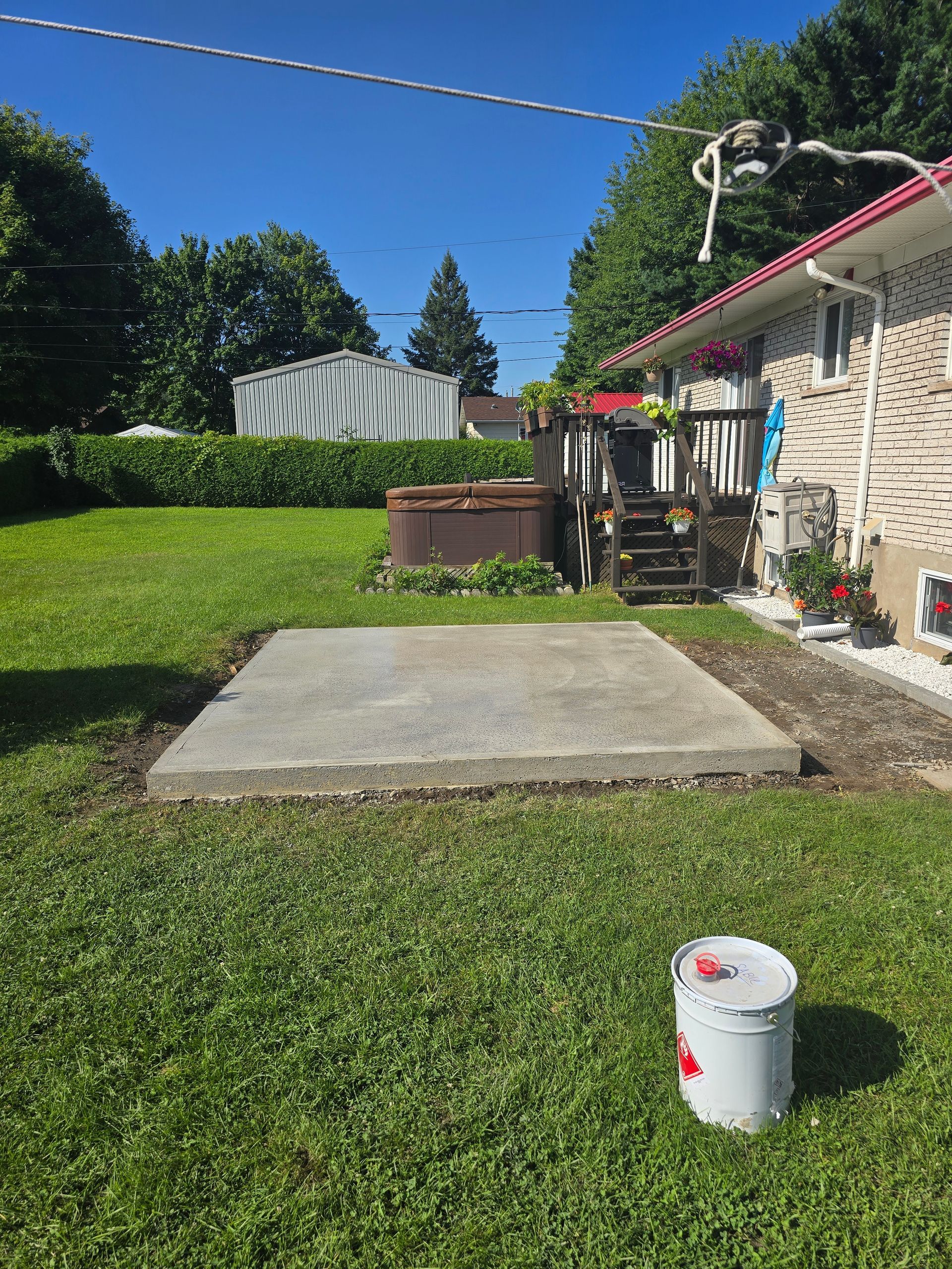 Un seau de peinture est posé dans l'herbe devant une maison.