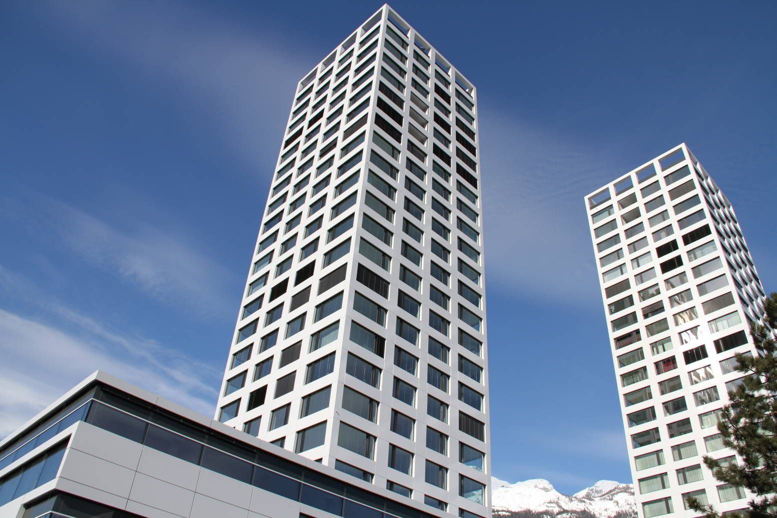 Zwei weisse Hochhäuser vor blauem Himmel mit Wolken.