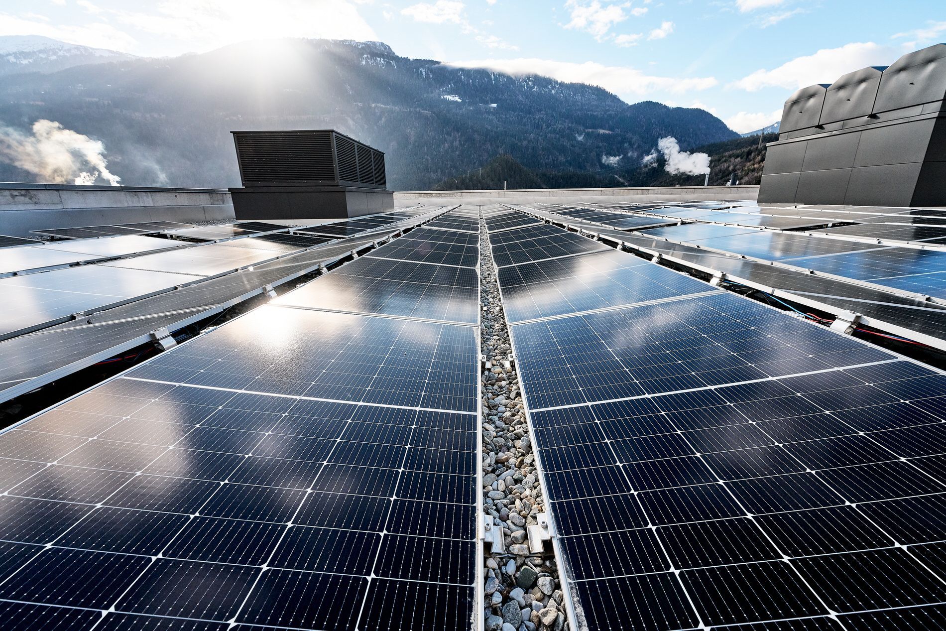 Eine Reihe von Solarmodulen auf einem Dach mit Bergen im Hintergrund