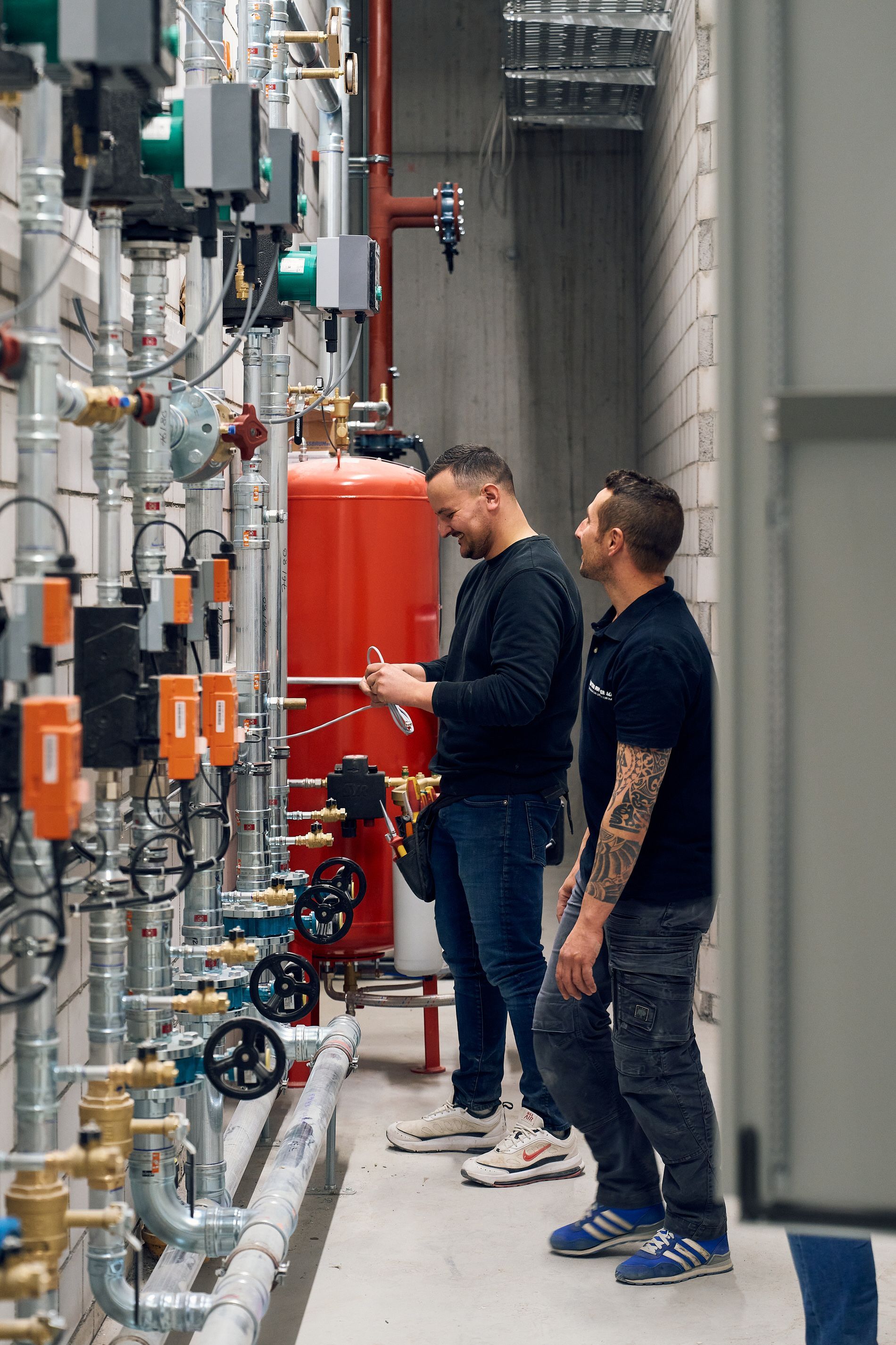 Zwei Männer arbeiten an einem Rohrleitungssystem in einem Gebäude.