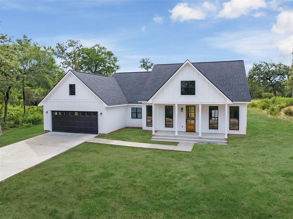 A white house with a black garage door is sitting on top of a lush green field.