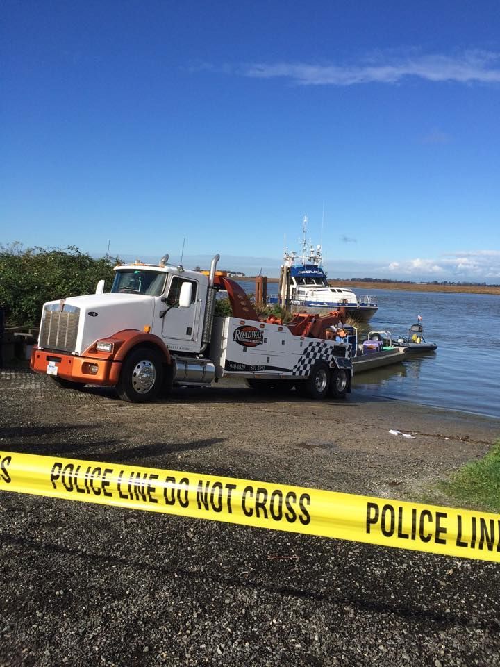 A white and orange tow truck parked on a boat ramp behind yellow