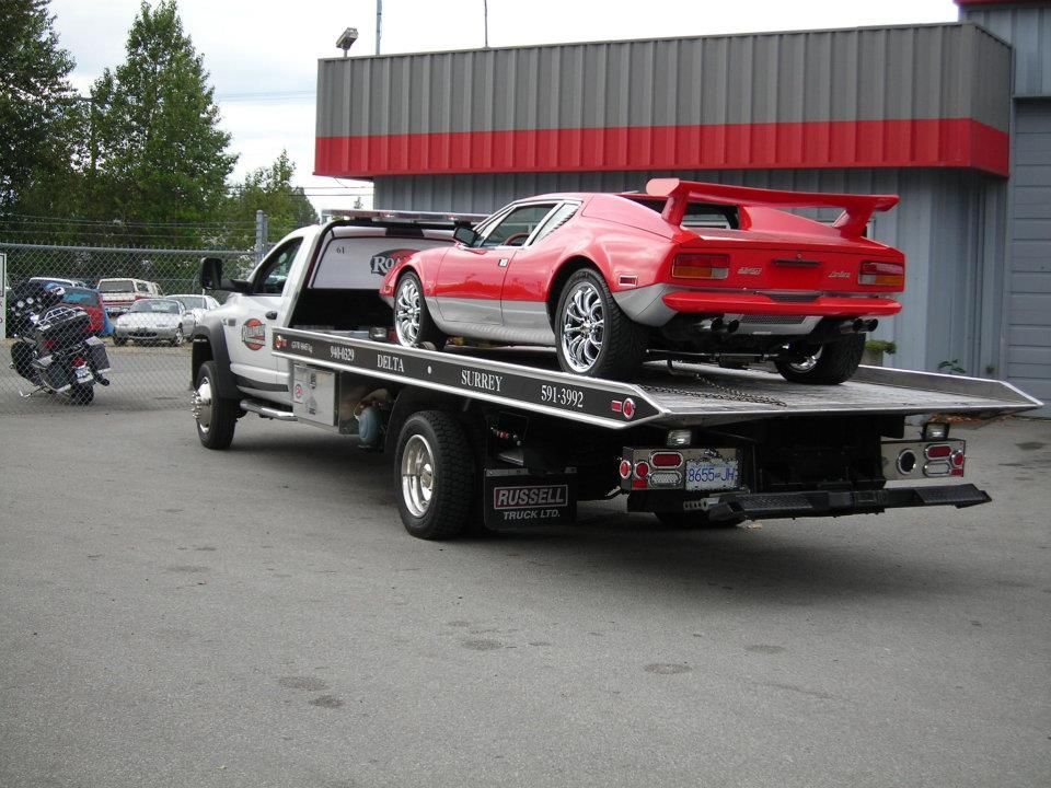 A bright red sports car on the flatbed of a tow truck parked in a lot, with a motorcycle parked nearby.