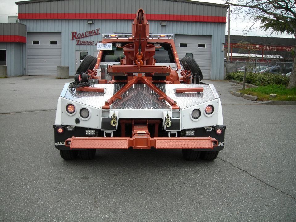 Rear view of a red and white heavy-duty tow truck parked on asphalt in front of a service center garage.