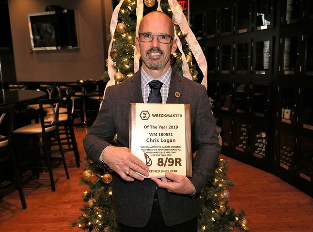 A man in a suit holds an award plaque in front of a decorated Christmas tree in a restaurant.