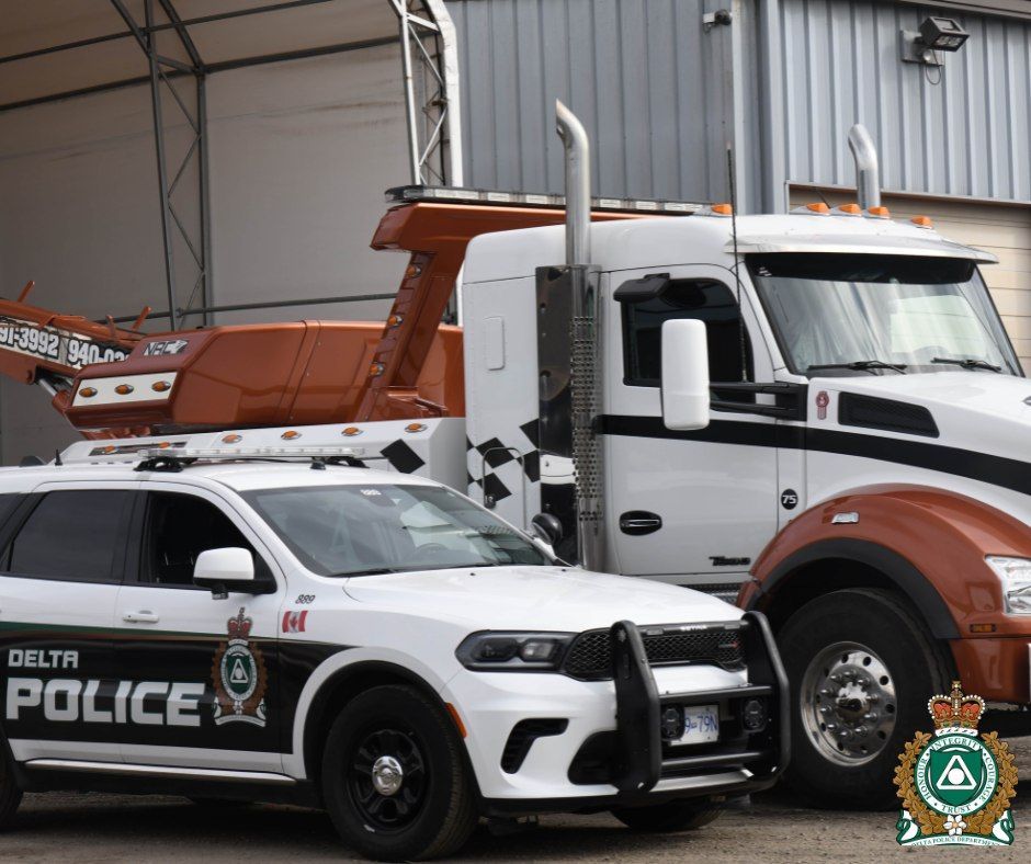 A white Delta Police SUV parked in front of a white and orange heavy-duty tow truck.