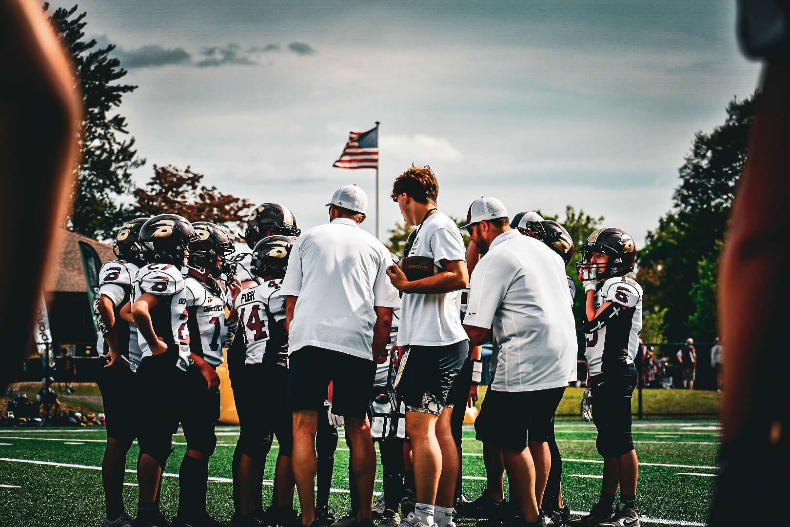 Football players huddle around a football, reaching hands together, blue sky backdrop.