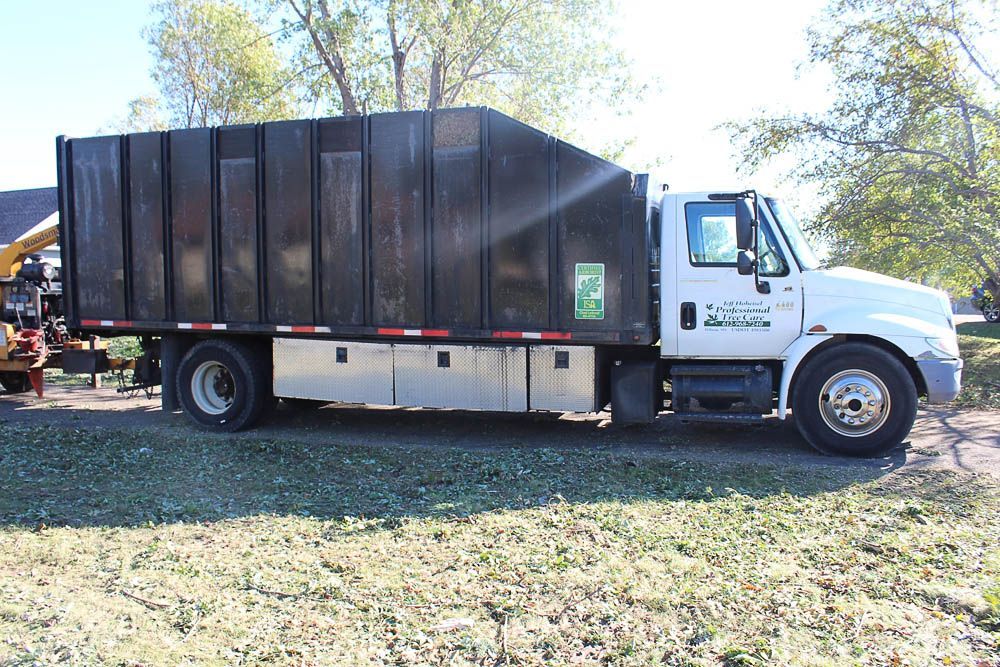 A white garbage truck is parked in a grassy field.