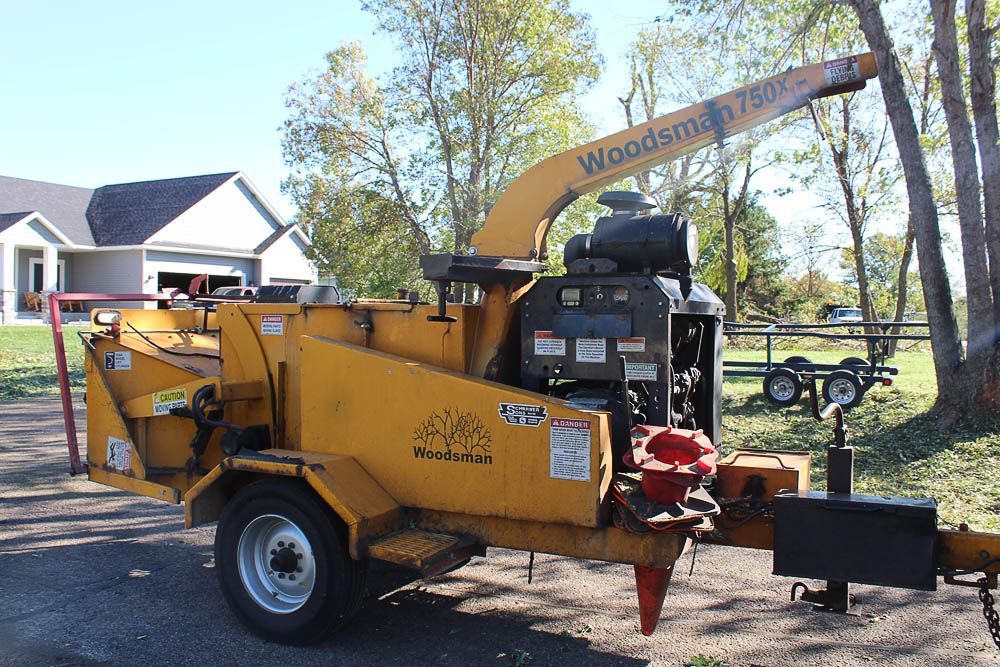 A yellow woodsman tree chipper is parked in front of a house