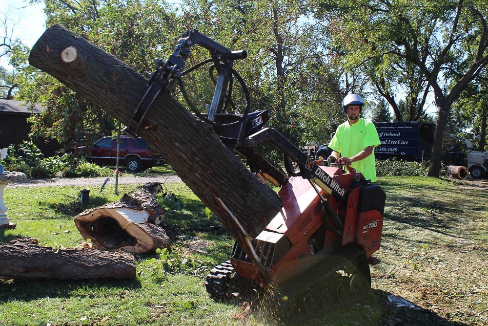A man is standing next to a machine that is cutting a tree