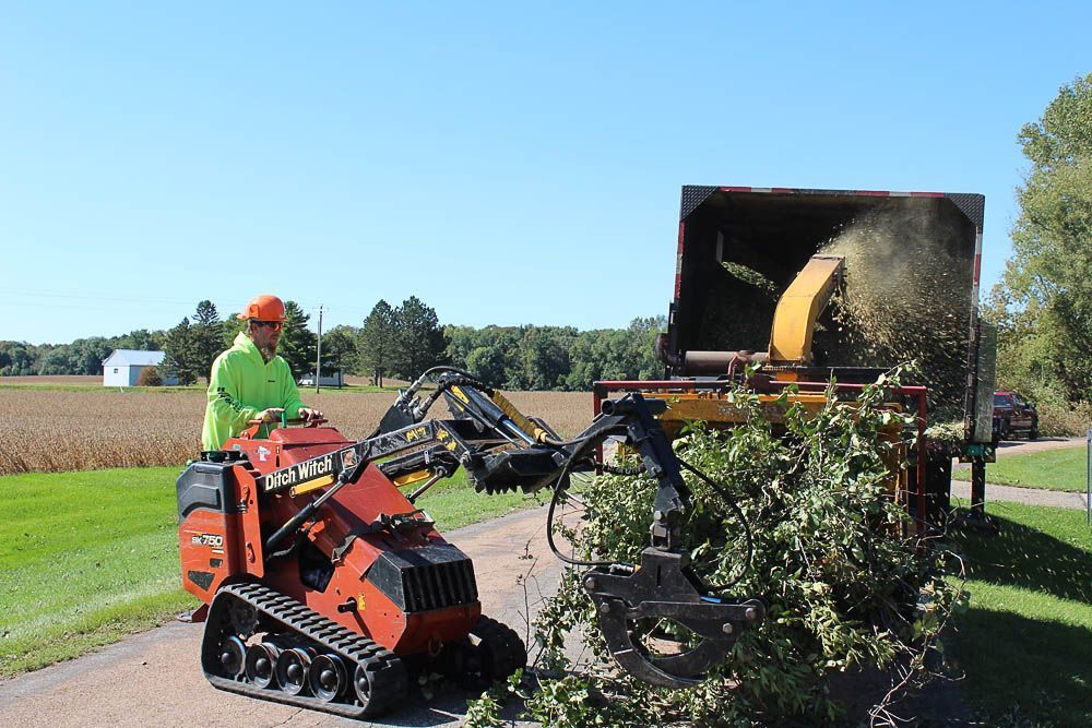 A man is standing next to a machine that is cutting trees.