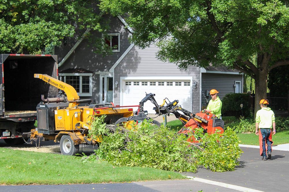 A man is standing next to a tree chipper in front of a house.